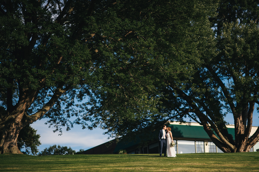 distant shot of bride and groom kissing on the ground of their country club wedding