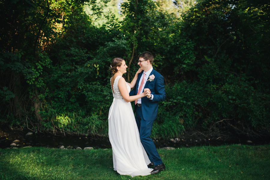 bride and groom smiling and dancing together near a small creek outdoors