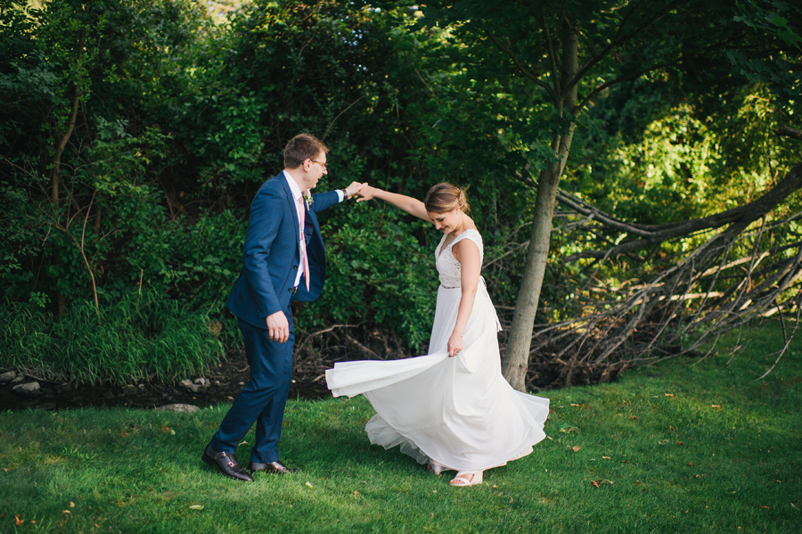 groom twirling his bride near a stream in a wooded area