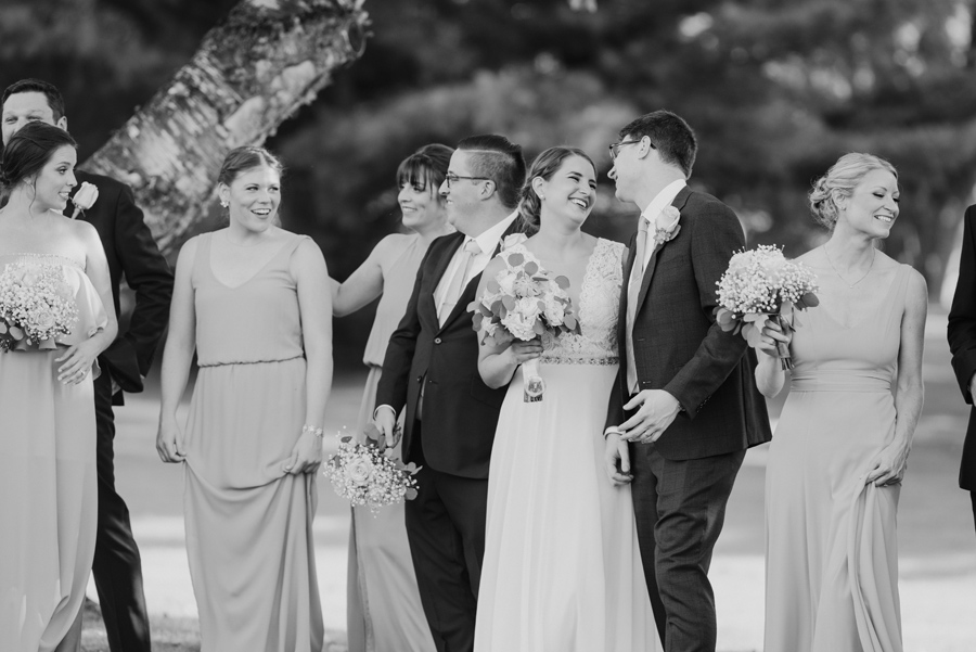 black and white of bride and groom laughing together while strolling with their wedding party