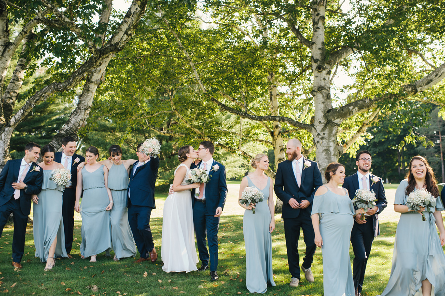 bride and groom kissing while their wedding party members stroll the grounds around them