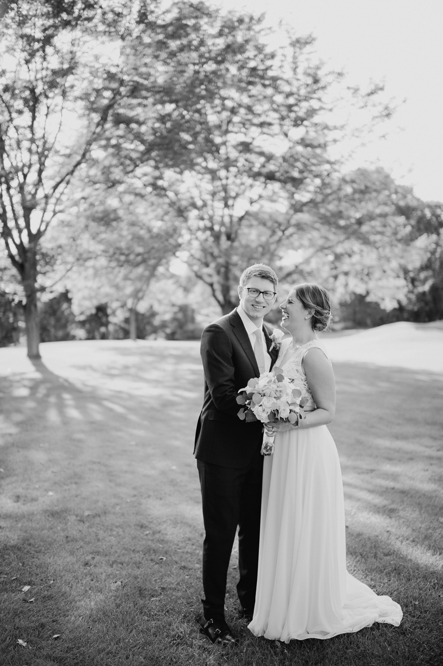 black and white portrait of groom smiling at the camera while bride laughs