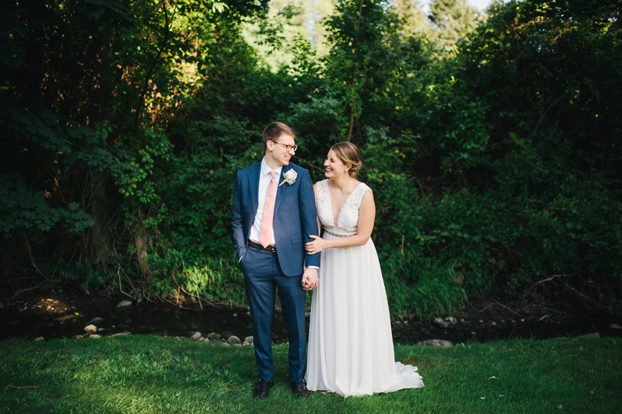 bride and groom laughing together and holding hangs in a lush wooded area