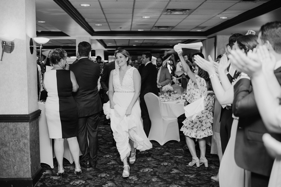 bride and groom running into wedding reception while guests cheer and waive dinner napkins in the air