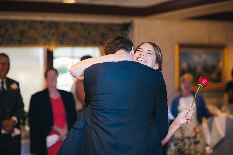 groom hugging a smiling bride after giving her a single red rose during their first dance