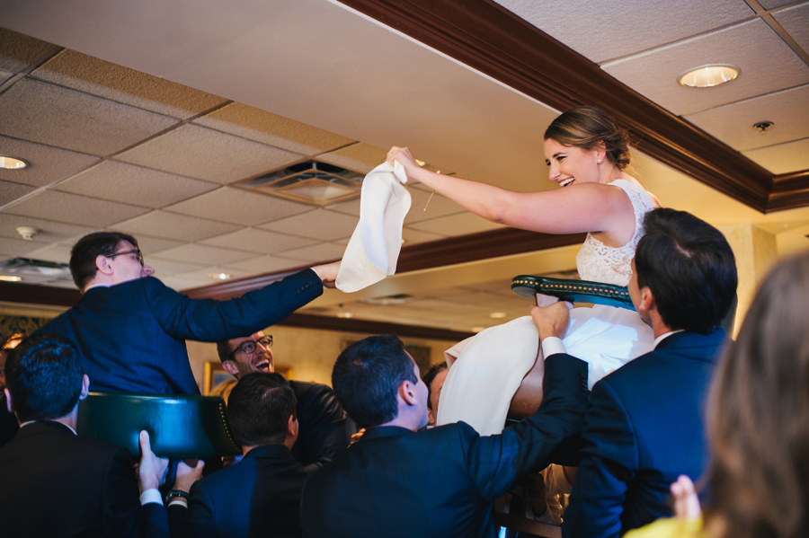 bride and groom being raised in chairs on the dance floor during the hora