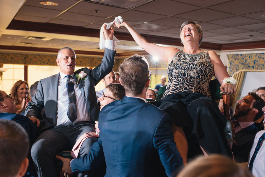 parents of the bride being raised in chairs during the hora and laughing