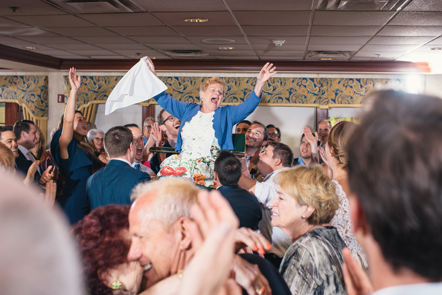 grandmother throwing her arms up while being raised in chair during the hora