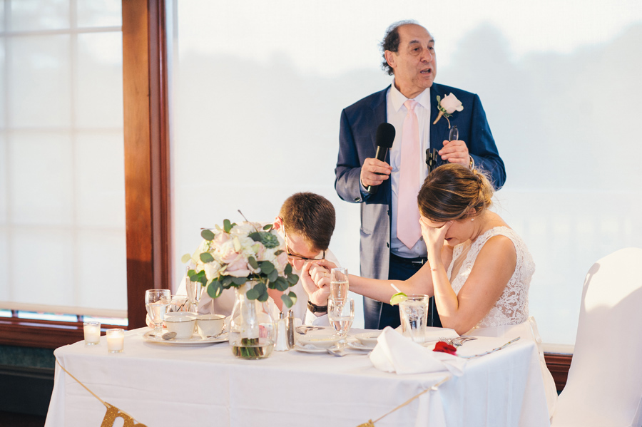 groom's father giving a blessing while couple bows heads at reception