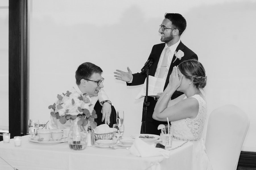 black and white of best man giving a speech while bride and groom laugh