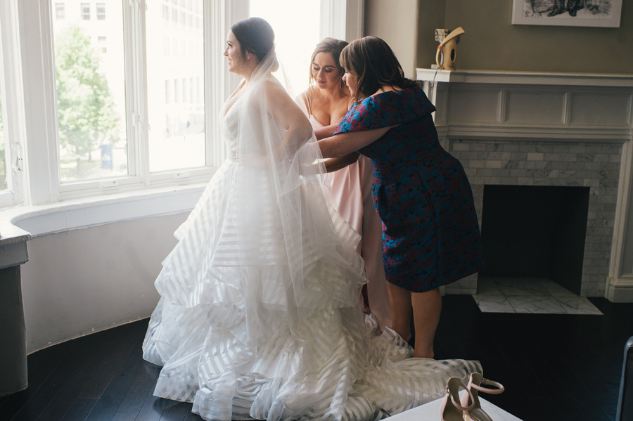 mother and sister of the bride zipping the bride into her dress