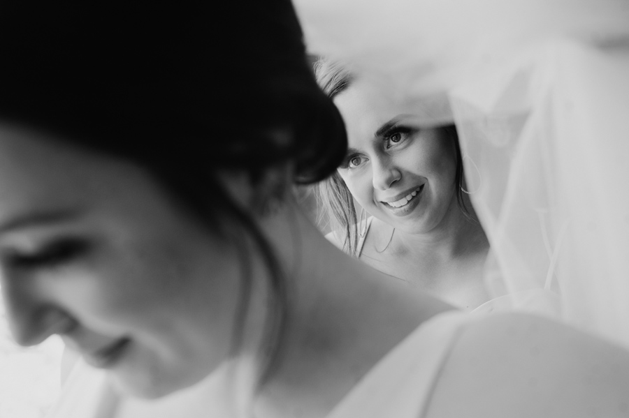 black and white shot of bridesmaid helping the bride under her veil