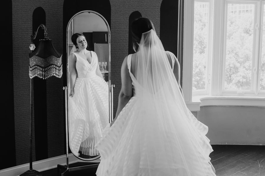 black and white of the bride smiling at herself in a full length mirror