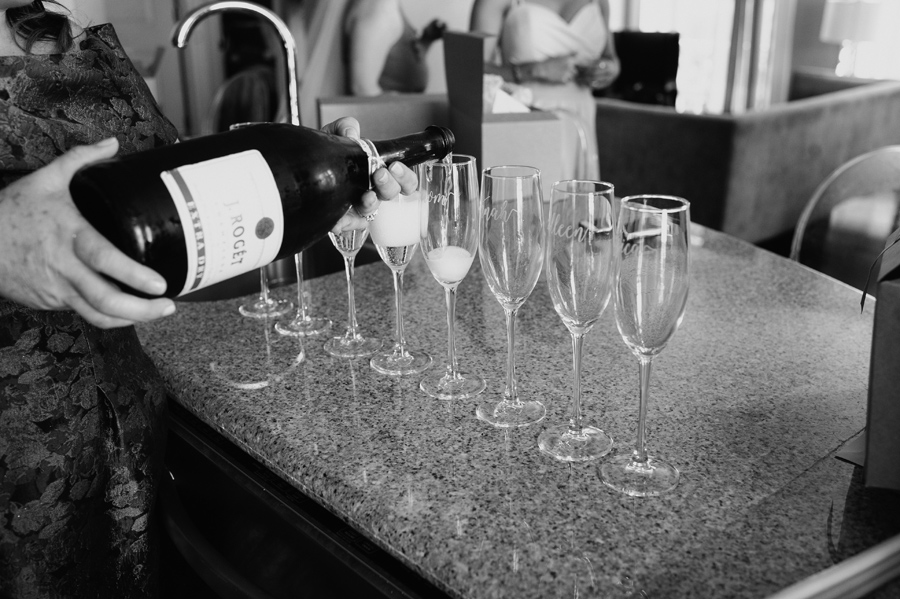 black and white pouring champagne into glass flutes with names engraved on them