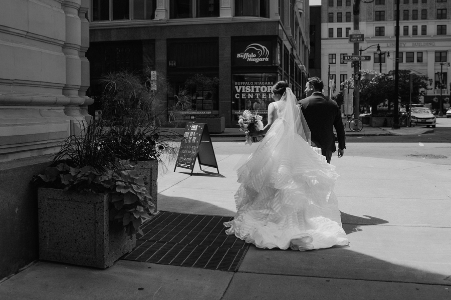 black and white of the bride and groom walking away from the camera around a corner on the street 