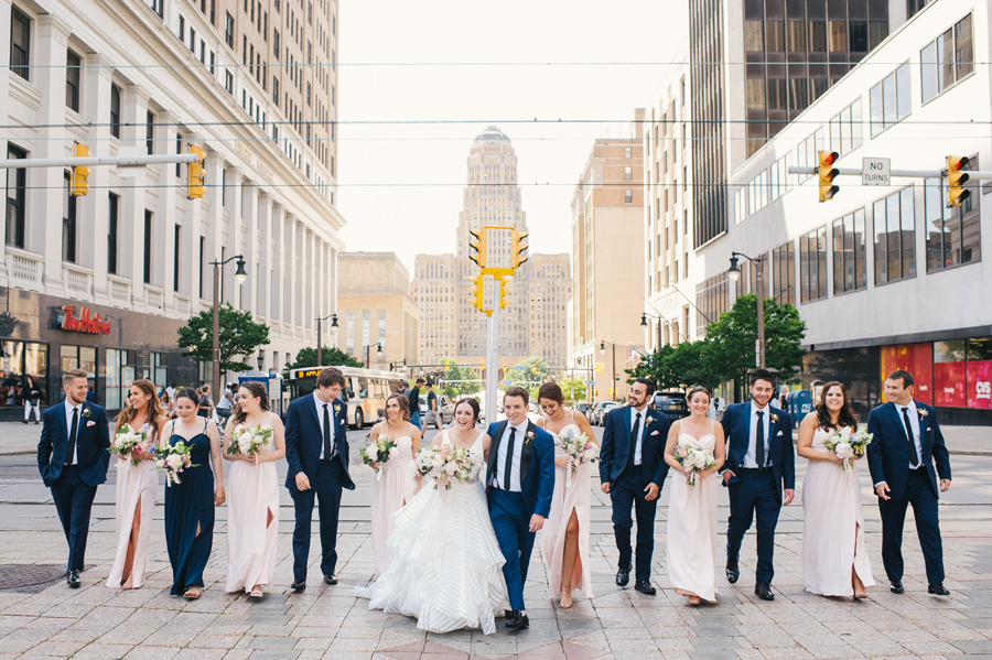 wedding party happily laughing and talking as they walk towards the camera on a brick paved street