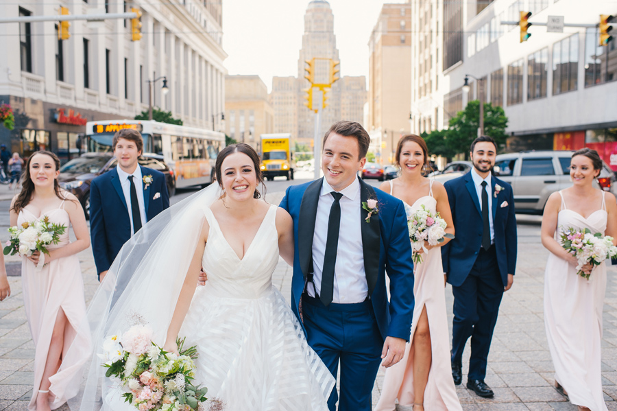 bride and groom walking towards the camera with arms around each other as bridal party follows