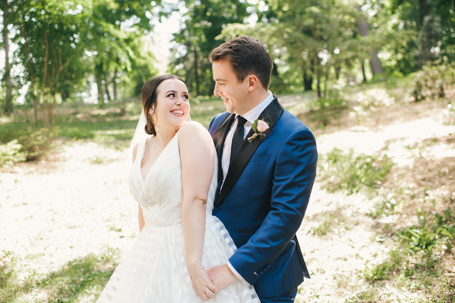 bride smiling over her shoulder at her groom as they hold hands