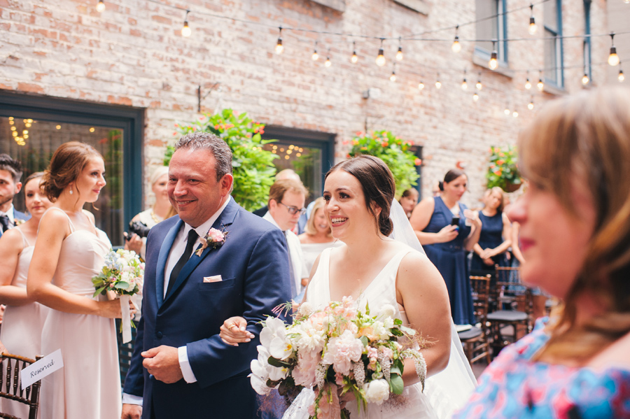 bride smiling at her groom as her dad escorts her down the aisle