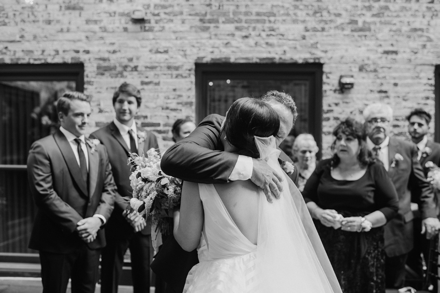 black and white of the father of the bride hugging her at the altar