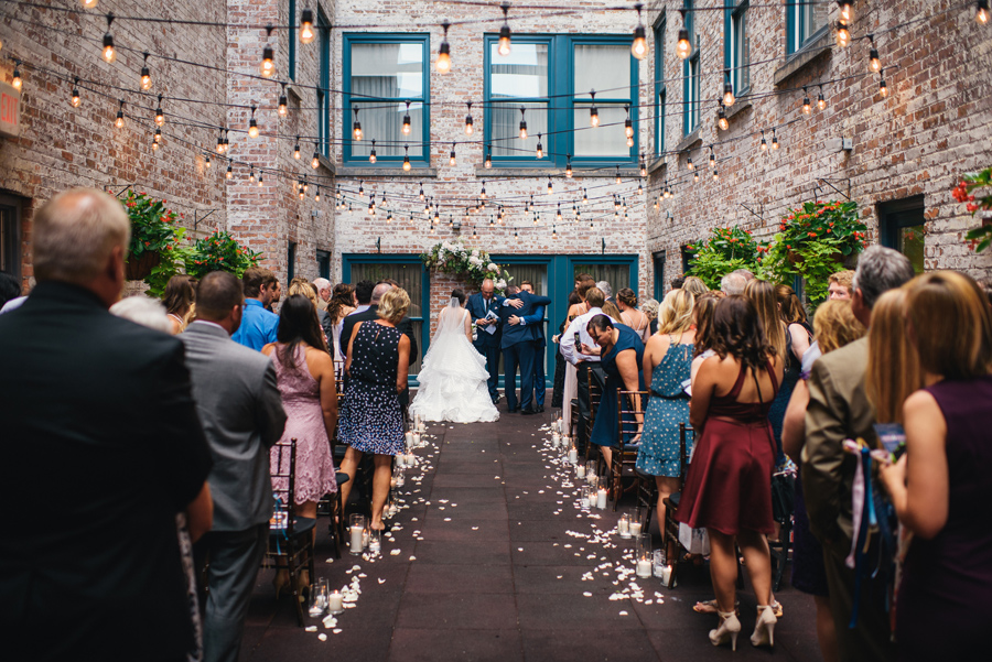 shot from the end of the aisle of the father of the bride hugging the groom after he gave his daughter away