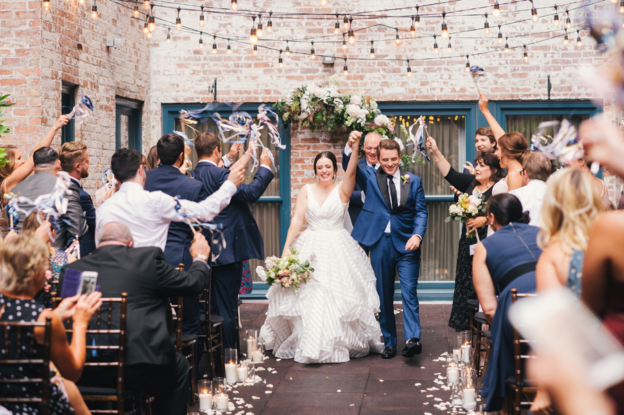 bride and groom walking back up the aisle while guests wave ribbon wands