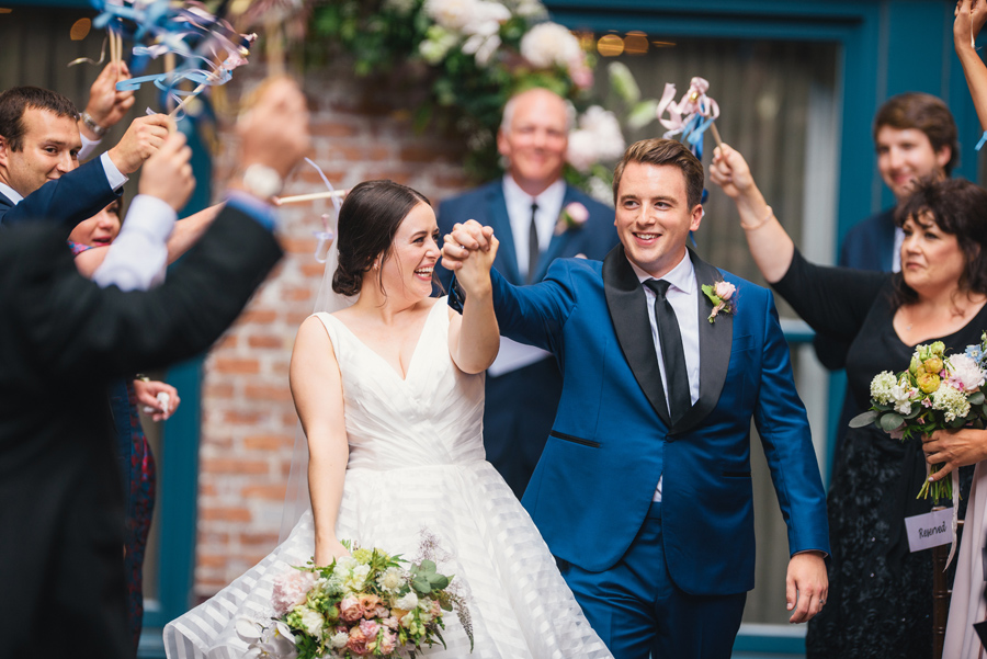 bride and groom hand in hand and arms raised as they walk back up the aisle together