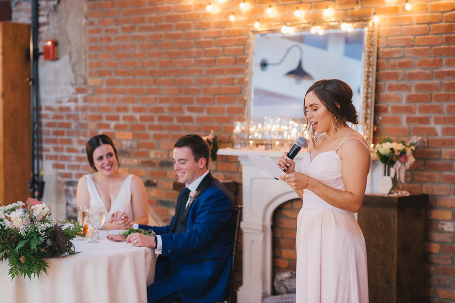 maid of honor giving her speech while bride and groom smile