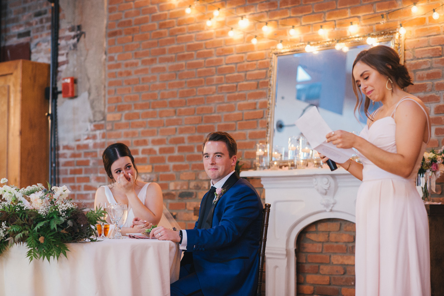 bride wiping tears away while maid of honor reads her speech