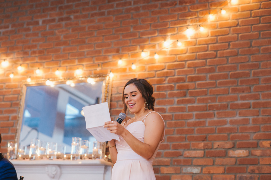 maid of honor smiling as she reads her speech during the wedding reception