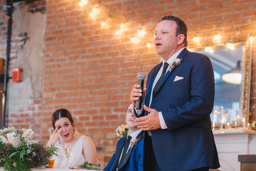 father of the bride giving a speech while the bride wipes away tears