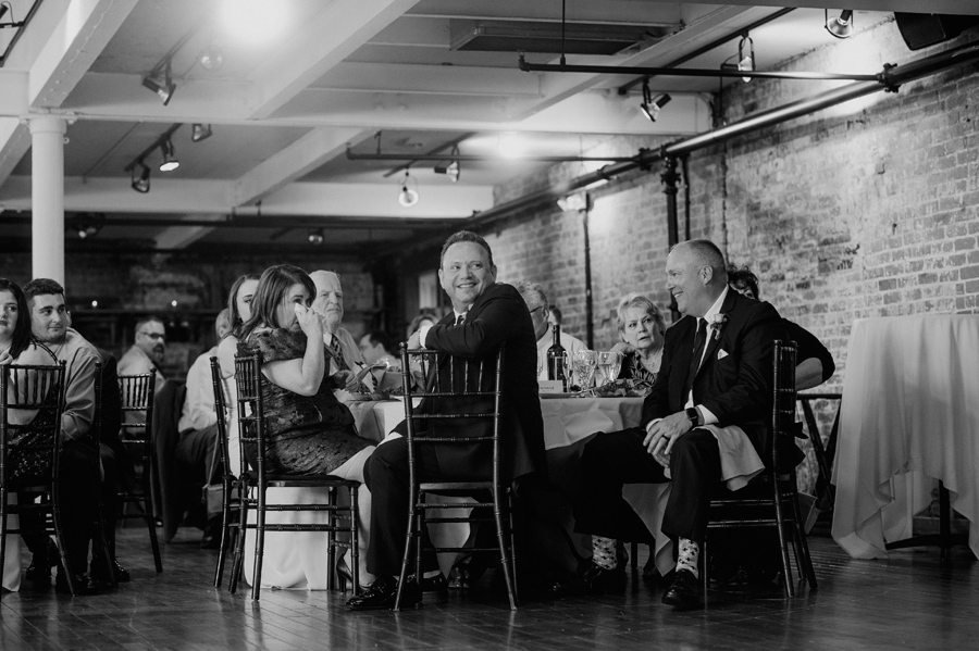 black and white of wedding guests smiling and crying during bride and groom's first dance