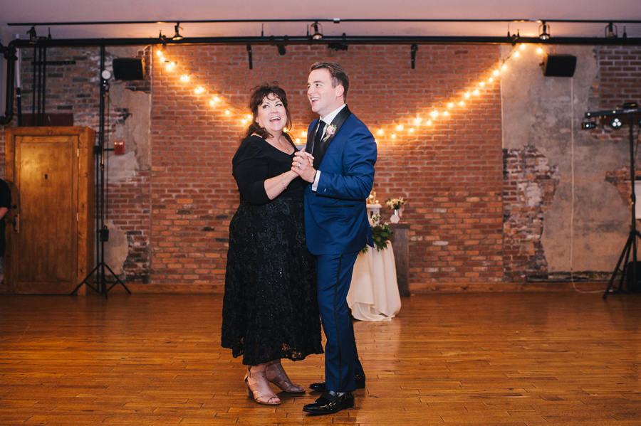 full length of the groom and his mother smiling during the mother son dance