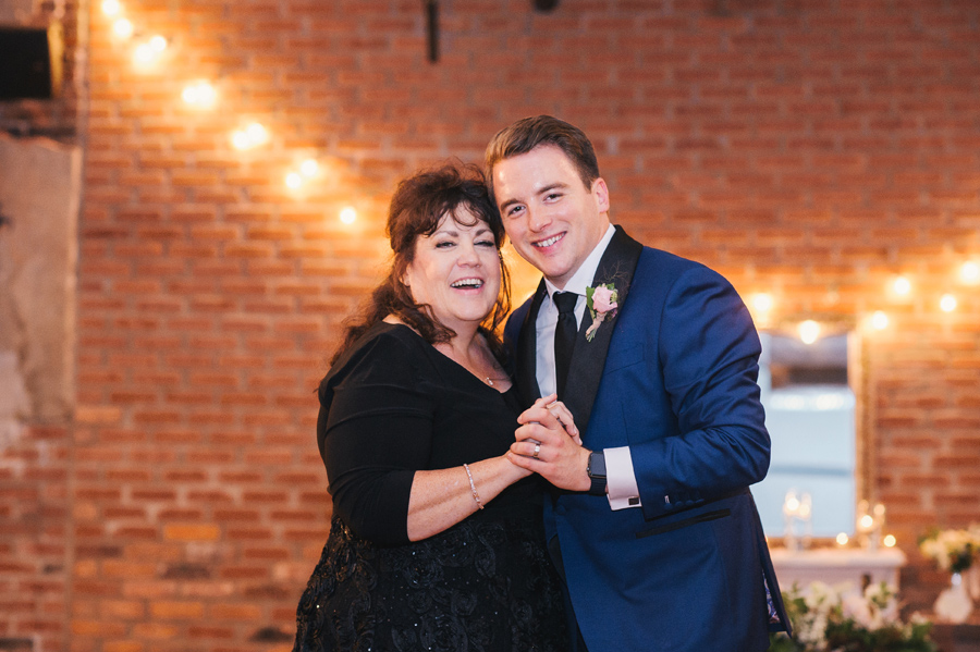 close shot of the mother of the groom and the groom smiling at the camera during their dance