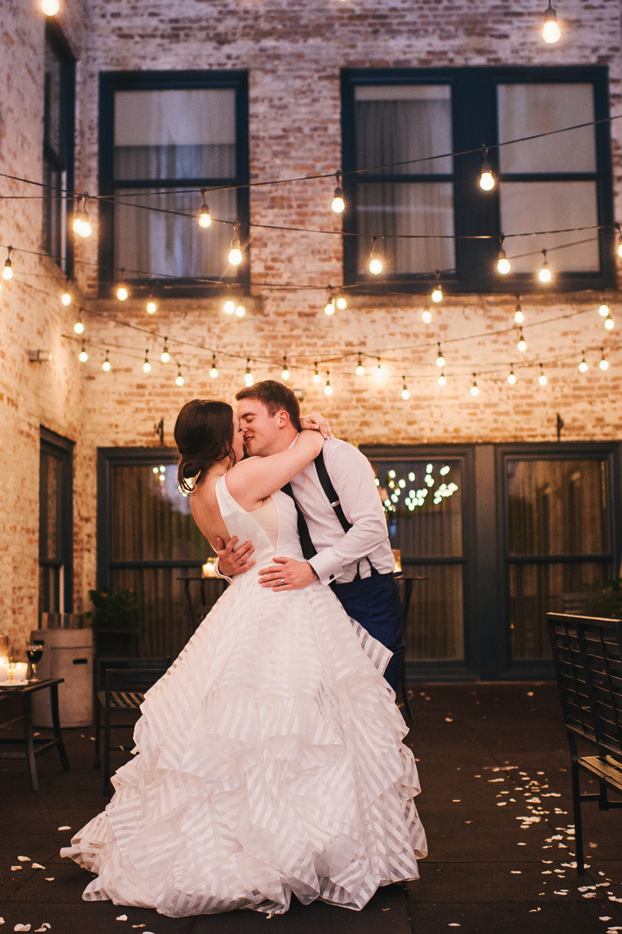 fill length of bride and groom leaning in for a kiss outdoors at night with twinkle lights in a brick wall courtyard