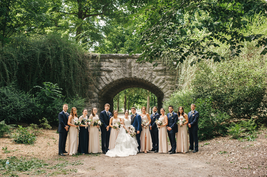 wedding party posing in front of a stone bridge in a heavily forested park