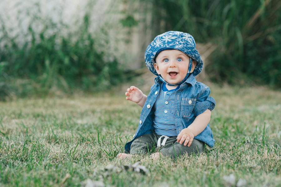 happy baby boy sitting in grass and smiling at camera