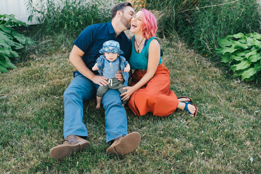 dad kissing mom's cheek as she laughs, baby in dad's lap