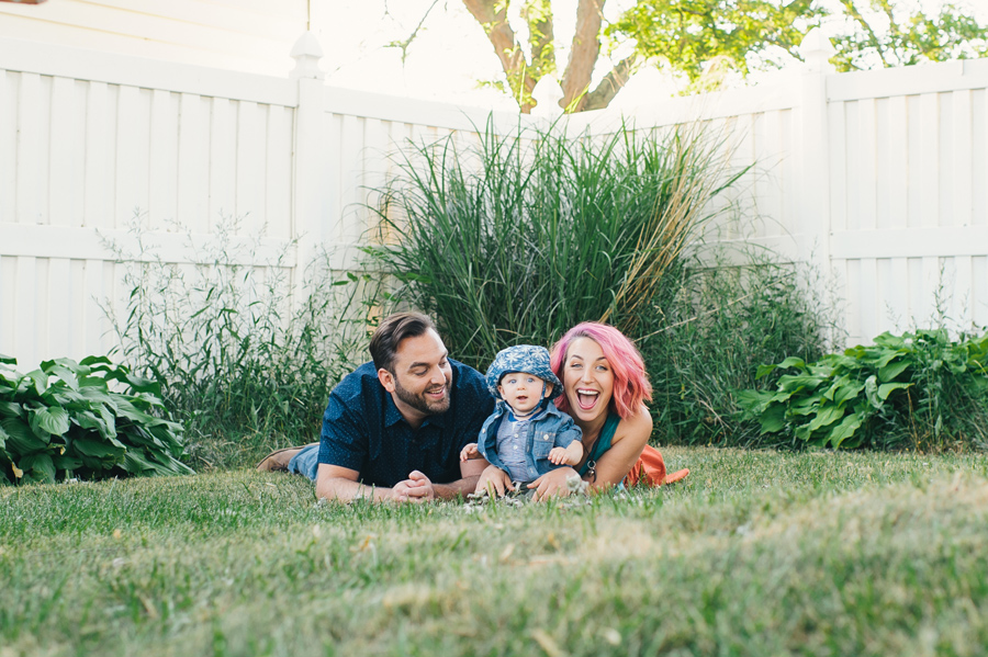 mom and dad laying on stomachs with baby son sitting on grass