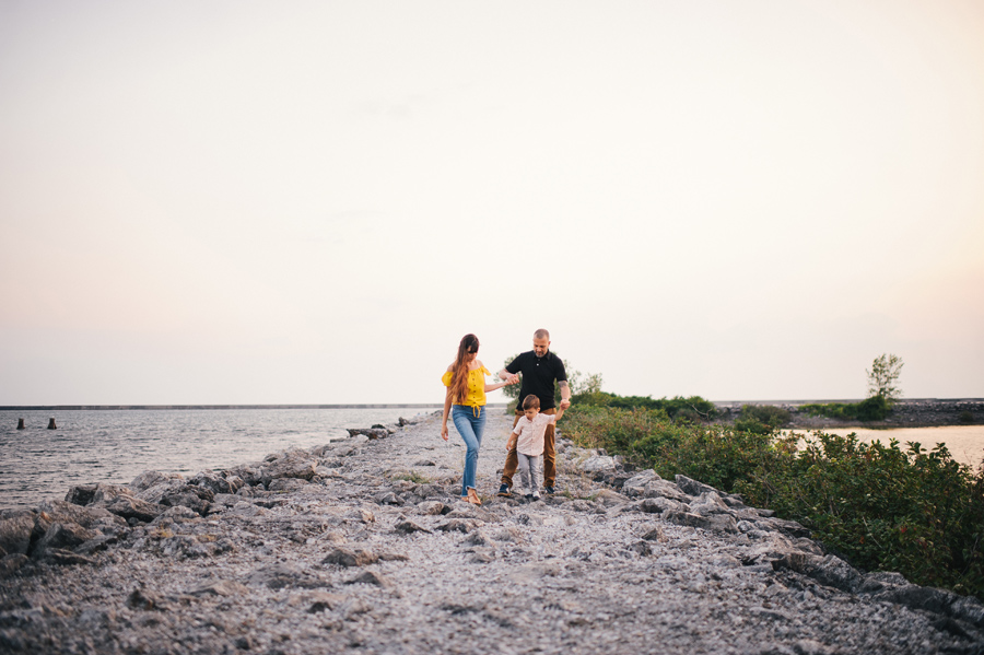 mom and dad helping son walk on rocks near the waterfront