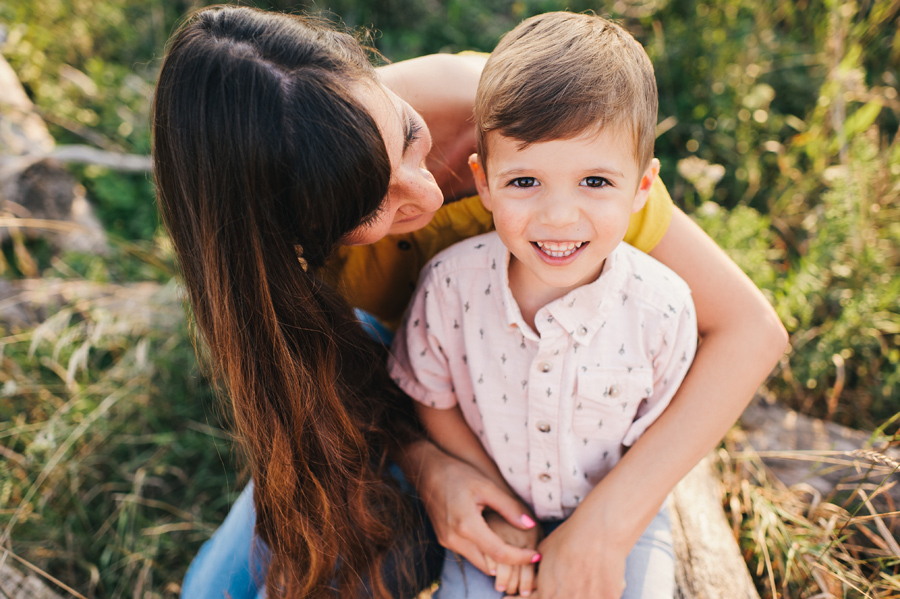 boy smiling at camera with mom's arms wrapped around him