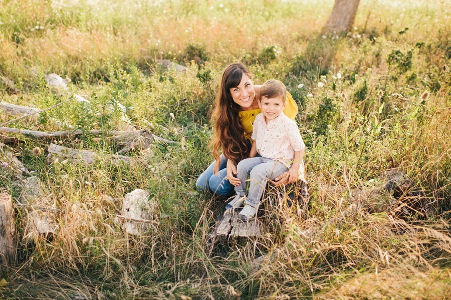 mom and son sitting on a log in a field smiling at camera