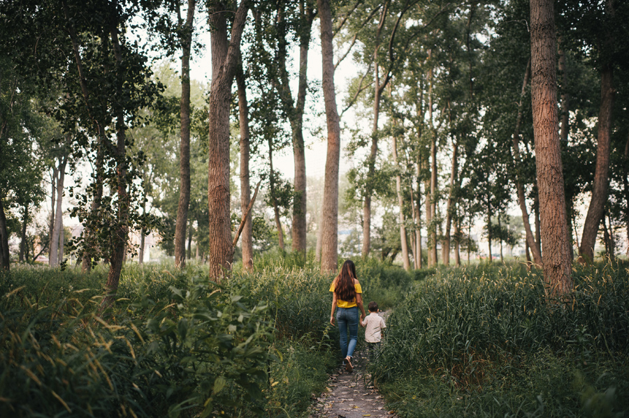 mom and son walking down a path through the woods headed away from camera