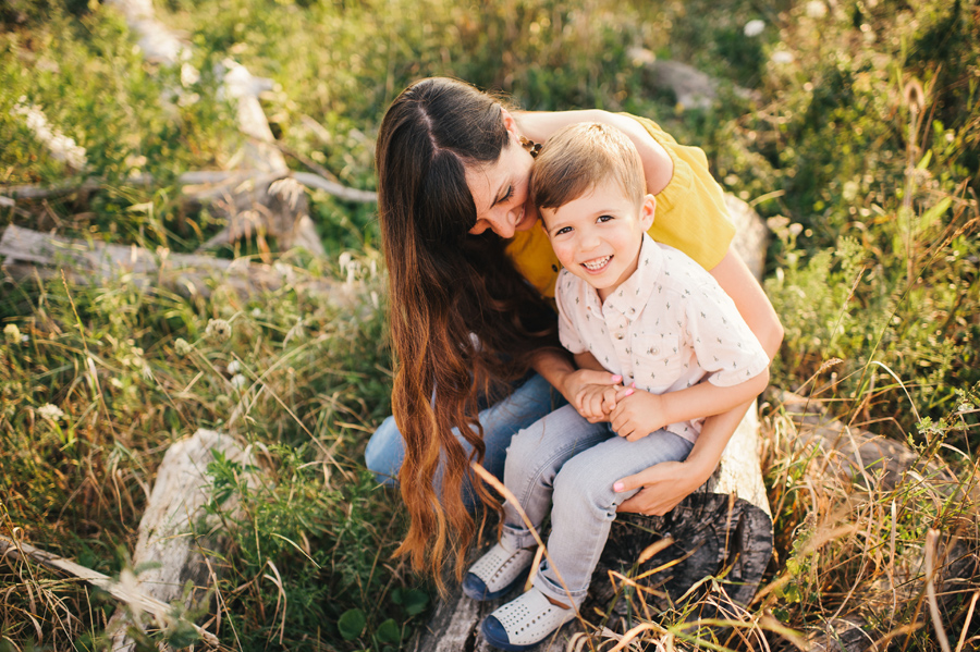 mom smiling with son while sitting together on a log