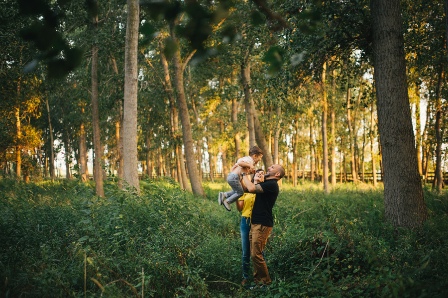 mother and father holding son up in the air in the woods at sunset